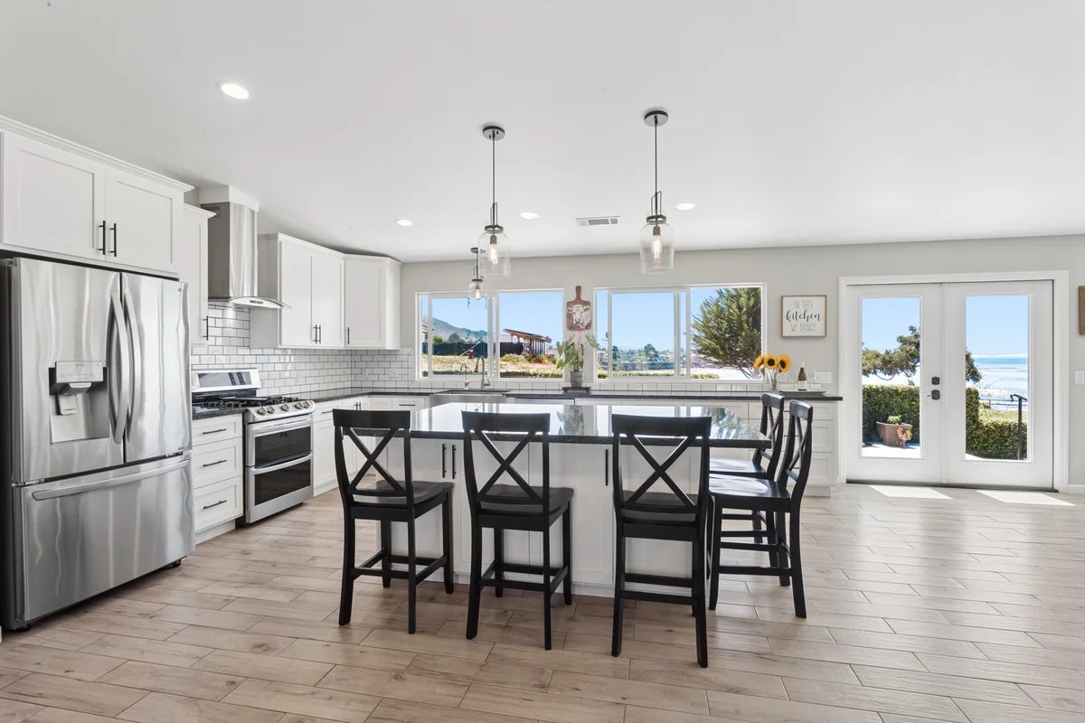 White kitchen with a broad island, dark stools and pendant lights.